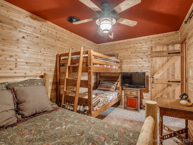 bedroom featuring a barn door, ceiling fan, wood walls, and light colored carpet