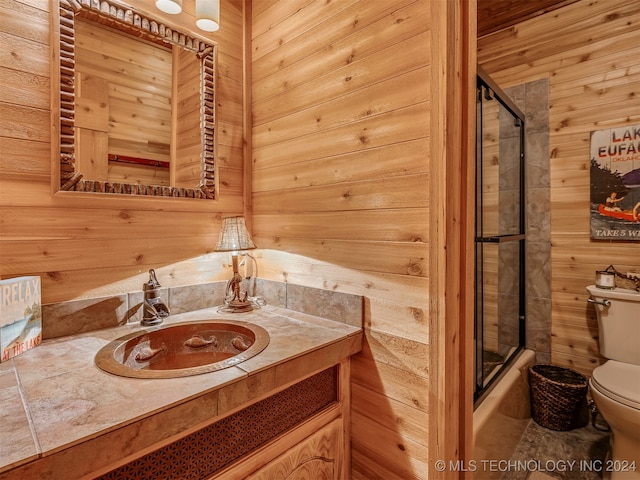 bathroom with vanity, walk in shower, wooden walls, and toilet