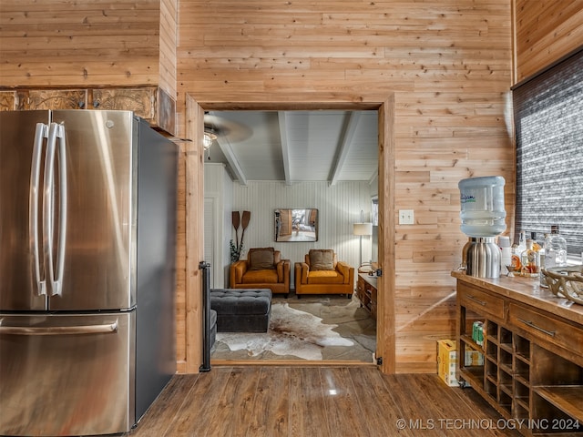 kitchen featuring wood walls, hardwood / wood-style flooring, stainless steel fridge, and beam ceiling