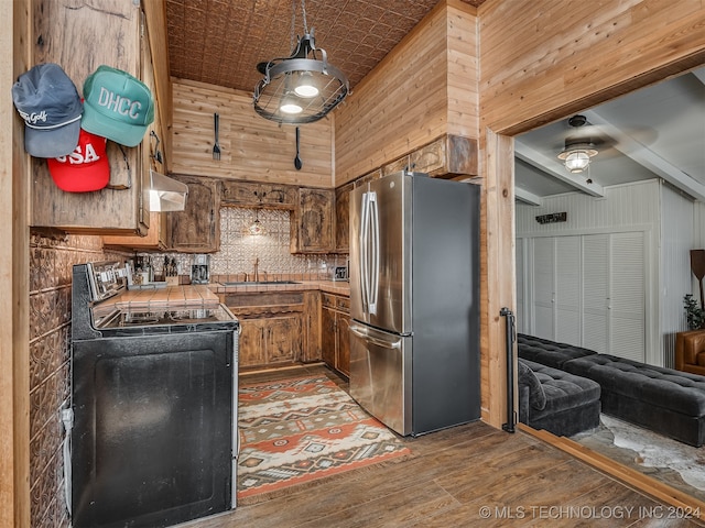 kitchen with tile countertops, stainless steel refrigerator, hardwood / wood-style flooring, electric range oven, and wooden walls