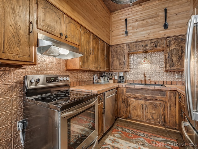 kitchen with wood walls, tile countertops, sink, appliances with stainless steel finishes, and tasteful backsplash