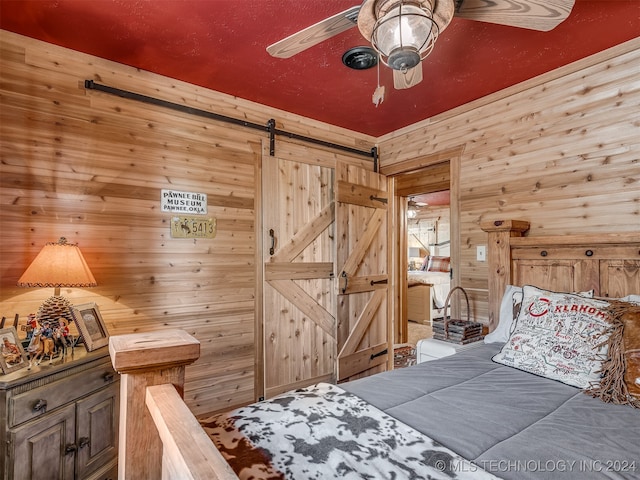 bedroom with a barn door, ceiling fan, and wooden walls