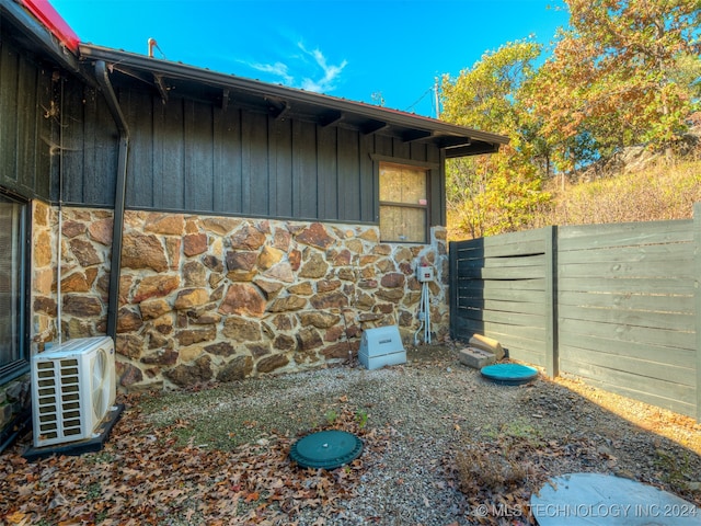 view of side of home with stone siding, fence, board and batten siding, and ac unit