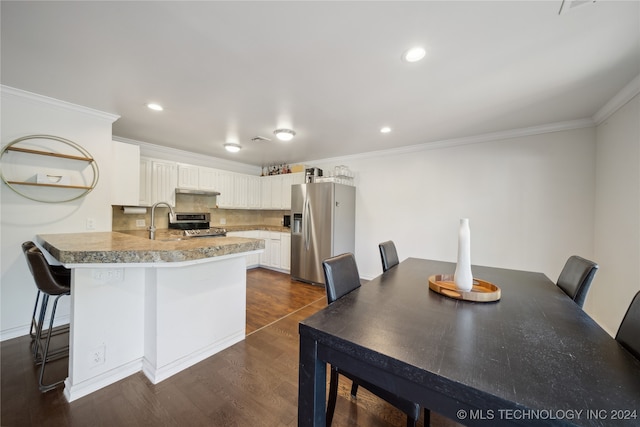 kitchen with kitchen peninsula, appliances with stainless steel finishes, a kitchen bar, white cabinets, and dark hardwood / wood-style flooring