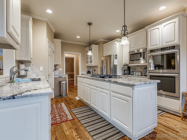 kitchen featuring stainless steel appliances, white cabinets, sink, pendant lighting, and light hardwood / wood-style flooring