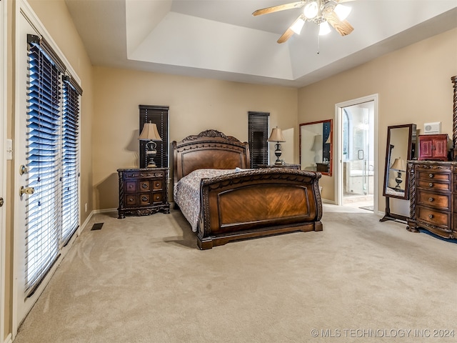 bedroom with ensuite bathroom, ceiling fan, light carpet, and a tray ceiling