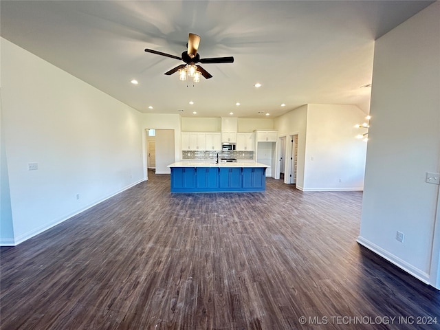 kitchen with ceiling fan with notable chandelier, dark wood-type flooring, white cabinets, tasteful backsplash, and an island with sink