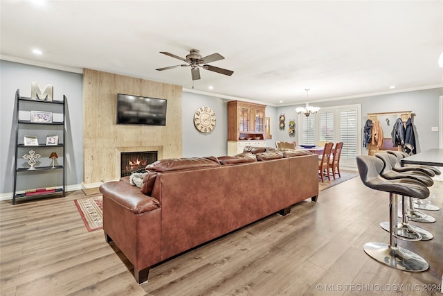 living room featuring a large fireplace, ceiling fan with notable chandelier, light hardwood / wood-style flooring, and ornamental molding