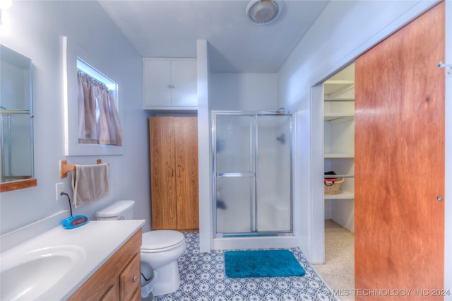 bathroom featuring a shower with door, vanity, and toilet