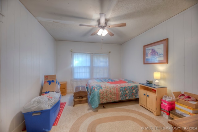 bedroom featuring a textured ceiling, ceiling fan, light colored carpet, and wood walls