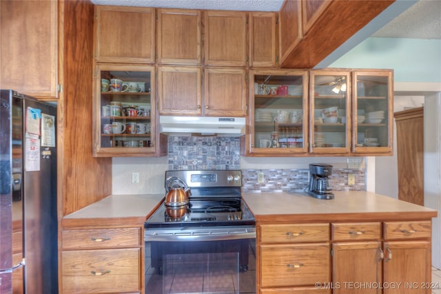 kitchen featuring stainless steel electric stove, decorative backsplash, black fridge, and a textured ceiling