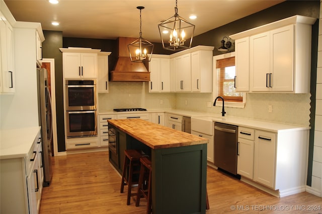 kitchen featuring a center island, custom range hood, butcher block countertops, white cabinetry, and appliances with stainless steel finishes