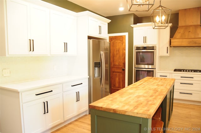 kitchen featuring stainless steel appliances, custom range hood, pendant lighting, white cabinets, and a center island