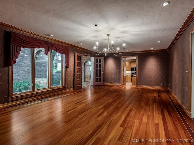 unfurnished living room featuring french doors, ornamental molding, a textured ceiling, a notable chandelier, and wood-type flooring