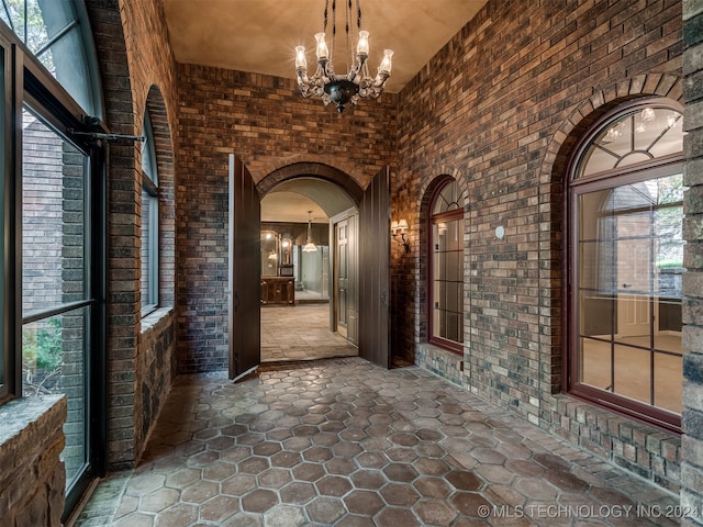 corridor featuring brick wall and a notable chandelier