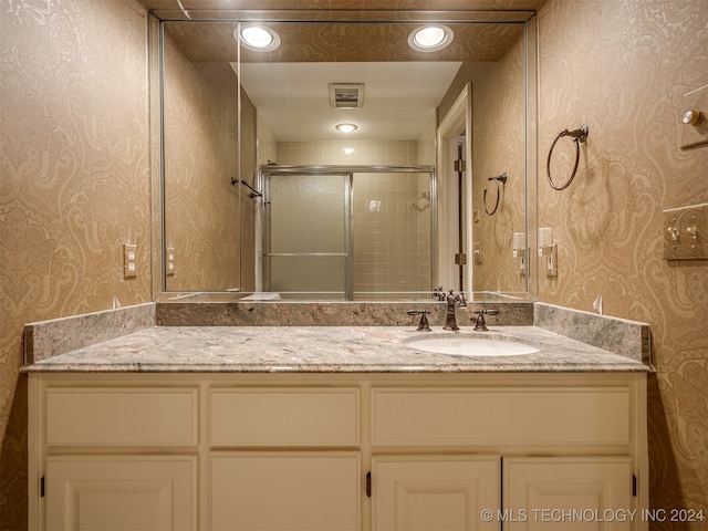 bathroom featuring a shower with door and vanity