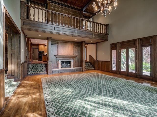 living room with beam ceiling, wood-type flooring, an inviting chandelier, a high ceiling, and wood walls