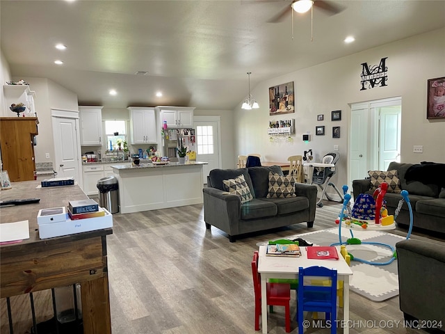 living room featuring ceiling fan with notable chandelier, light wood-type flooring, and lofted ceiling