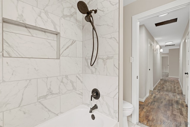 bathroom with wood-type flooring, tiled shower / bath combo, and toilet