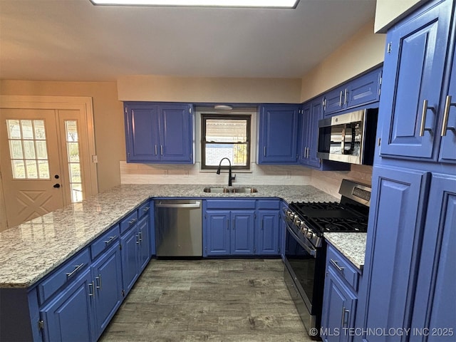 kitchen featuring light stone countertops, sink, blue cabinets, kitchen peninsula, and appliances with stainless steel finishes