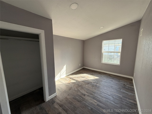 unfurnished bedroom featuring dark hardwood / wood-style floors, vaulted ceiling, and a closet