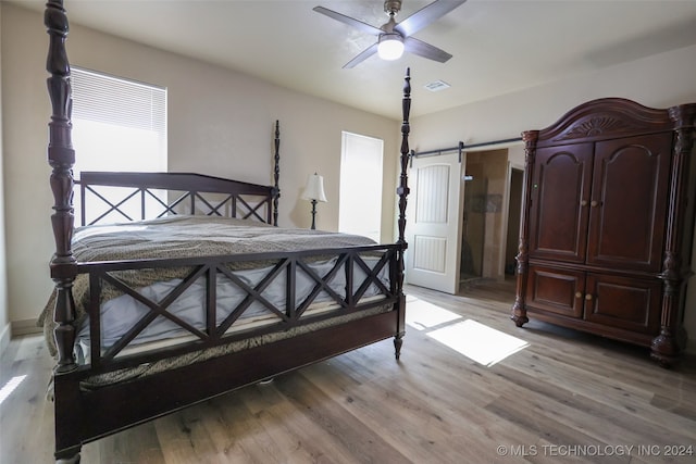 bedroom featuring light hardwood / wood-style flooring, a barn door, and ceiling fan