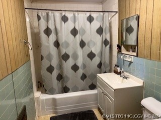 full bathroom with shower / bath combo, tile walls, wood walls, and vanity