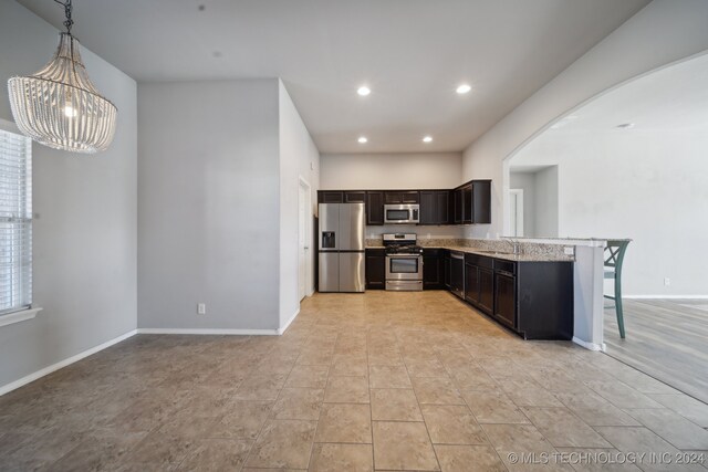 kitchen featuring light stone counters, stainless steel appliances, pendant lighting, sink, and a kitchen breakfast bar