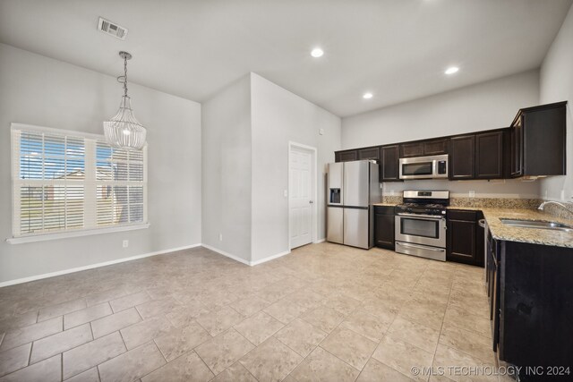 kitchen with light stone counters, stainless steel appliances, a notable chandelier, hanging light fixtures, and sink