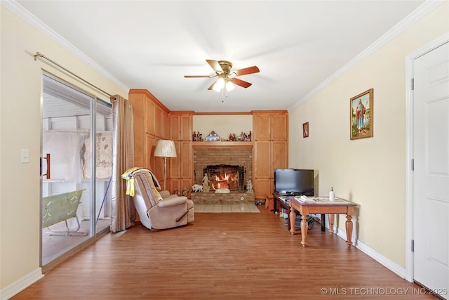 living area featuring ceiling fan, a brick fireplace, wood-type flooring, and crown molding