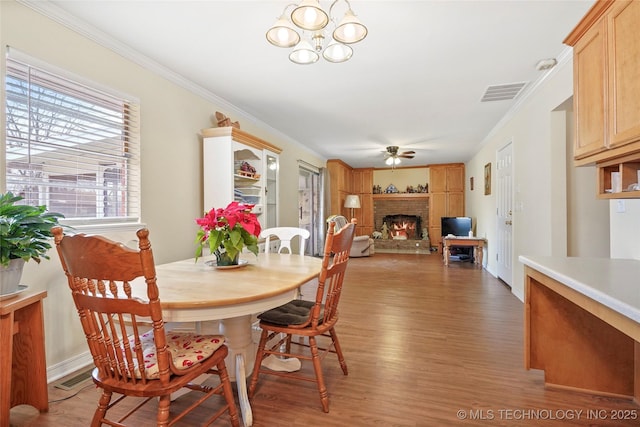 dining room featuring a brick fireplace, hardwood / wood-style floors, crown molding, and ceiling fan with notable chandelier