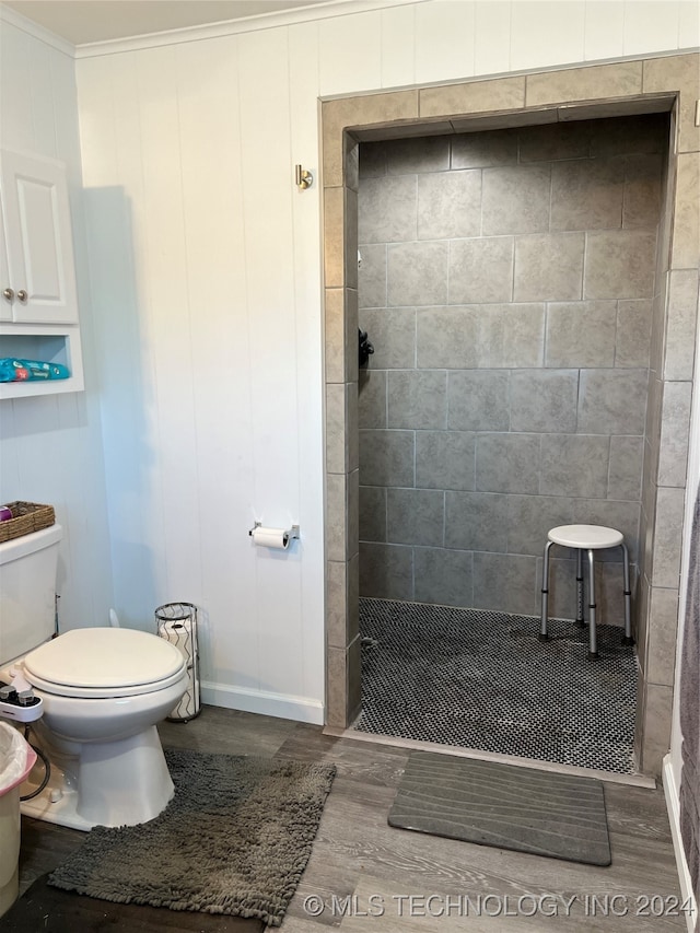 bathroom featuring hardwood / wood-style floors, toilet, tiled shower, and ornamental molding