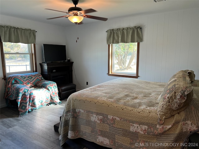 bedroom featuring wood walls, hardwood / wood-style flooring, ceiling fan, and multiple windows