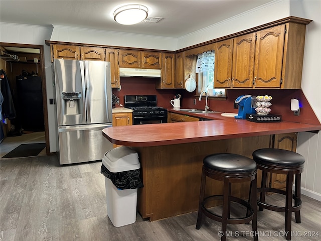 kitchen featuring black gas range, a kitchen bar, wood-type flooring, and stainless steel fridge with ice dispenser