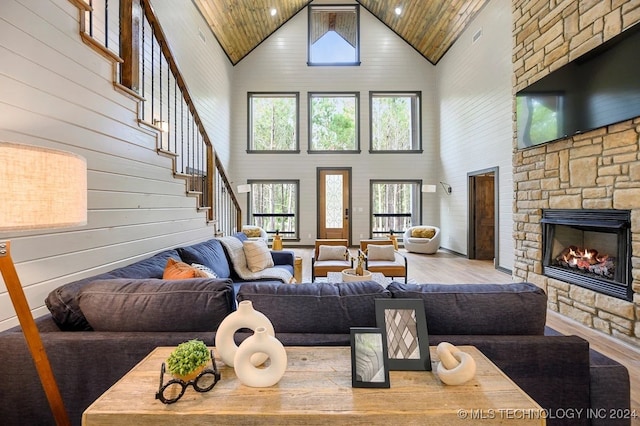 living room featuring a stone fireplace, wood-type flooring, wood ceiling, wooden walls, and high vaulted ceiling