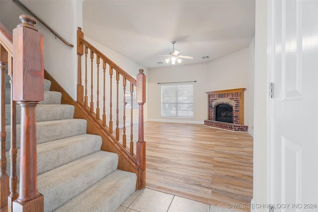 staircase featuring wood-type flooring, ceiling fan, and a brick fireplace