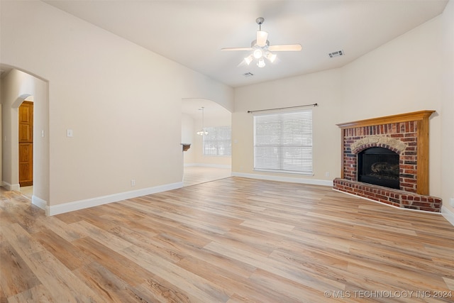 unfurnished living room featuring a brick fireplace, ceiling fan with notable chandelier, and light wood-type flooring