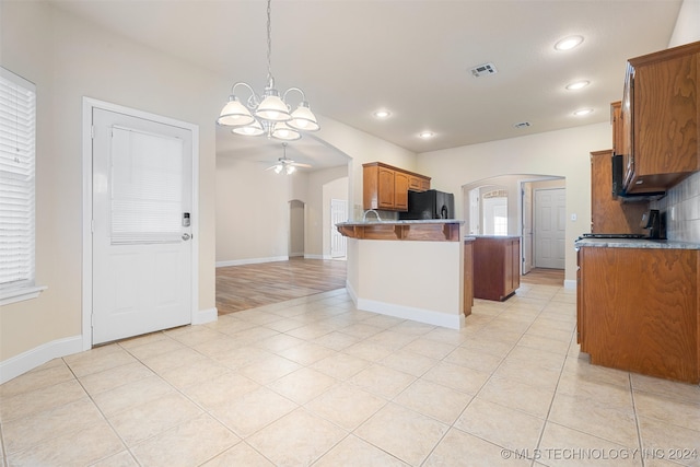 kitchen featuring black fridge, decorative light fixtures, light tile patterned floors, kitchen peninsula, and ceiling fan with notable chandelier