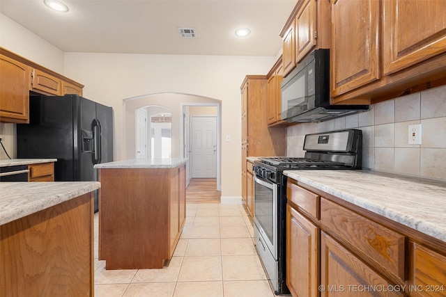 kitchen featuring black appliances, light tile patterned flooring, backsplash, light stone countertops, and a center island