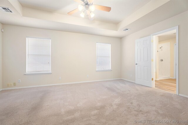 spare room featuring light colored carpet, ceiling fan, and a raised ceiling