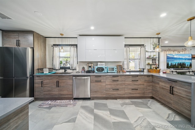 kitchen with sink, hanging light fixtures, stainless steel appliances, white cabinets, and decorative backsplash