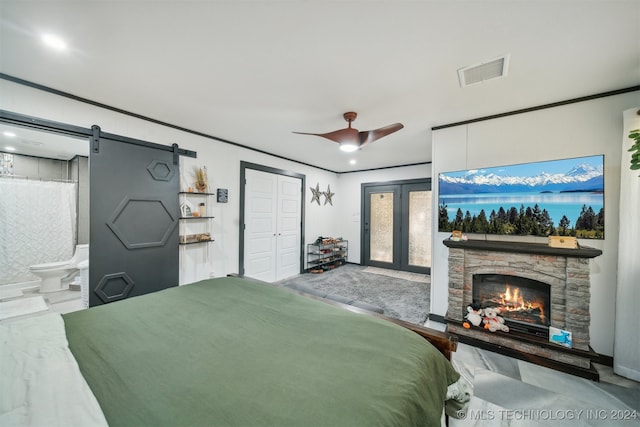 bedroom with connected bathroom, a stone fireplace, a closet, ceiling fan, and a barn door