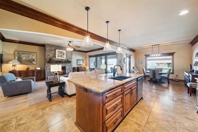 kitchen featuring stainless steel dishwasher, sink, decorative light fixtures, ornamental molding, and an island with sink