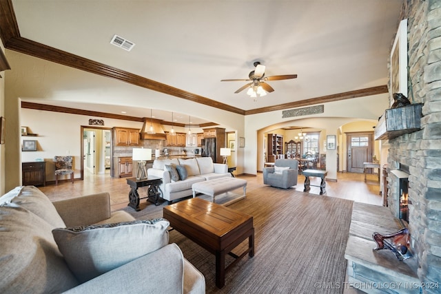 living room with ceiling fan, light wood-type flooring, crown molding, and a fireplace