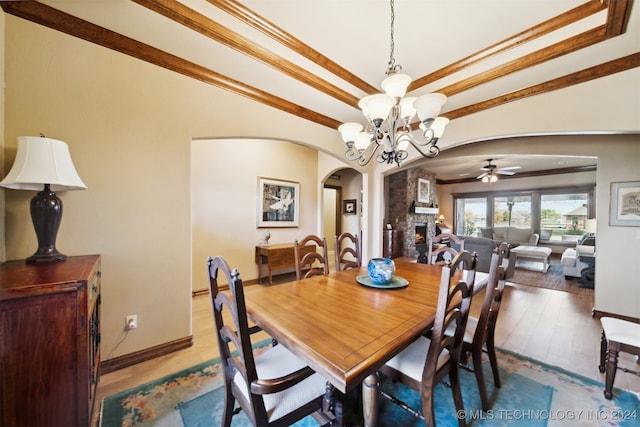 dining area featuring ceiling fan with notable chandelier, hardwood / wood-style floors, ornamental molding, and a stone fireplace