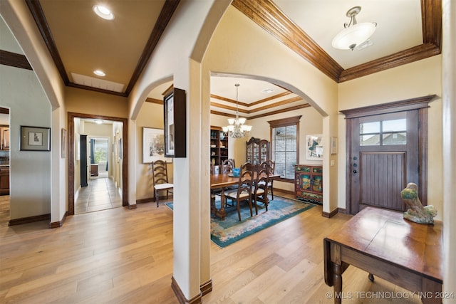 foyer with crown molding, light wood-type flooring, and an inviting chandelier