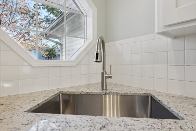 details featuring light stone countertops, backsplash, and sink