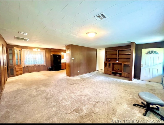 unfurnished living room with wood walls and light colored carpet