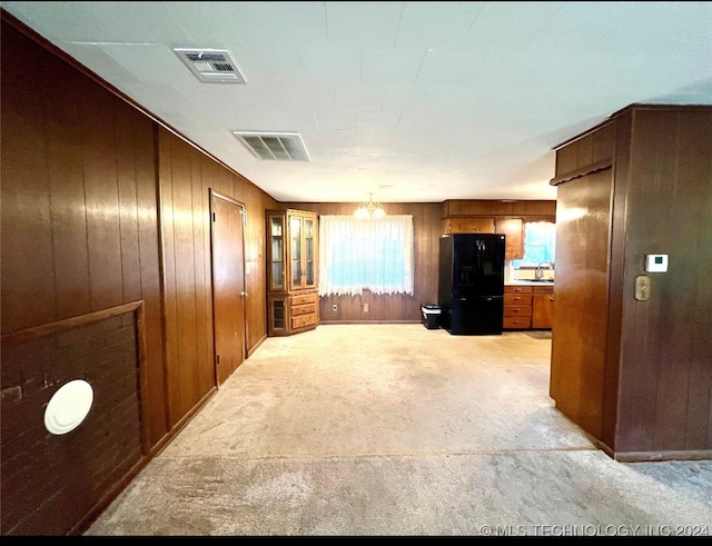 unfurnished living room with wood walls, a chandelier, sink, and light colored carpet