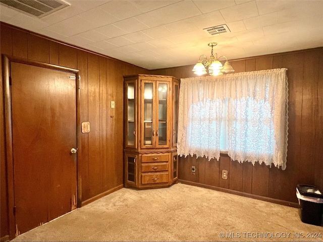 unfurnished dining area featuring wooden walls, light carpet, and a notable chandelier